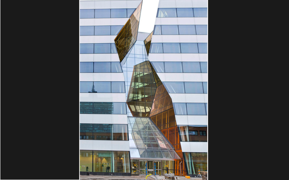 En kontorsbyggnad i kubisk form med stora glaspartier. I mitten av byggnaden är det en öppning i fasaden från marken upp mot taket. 