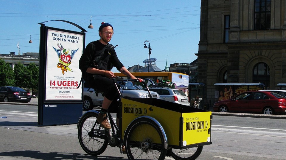 En man cyklar en gul lådcykel i stadsmiljö