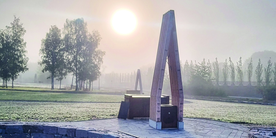 Träskulptur på stenlagd yta med gräsytor runtomkring en disig morgon.