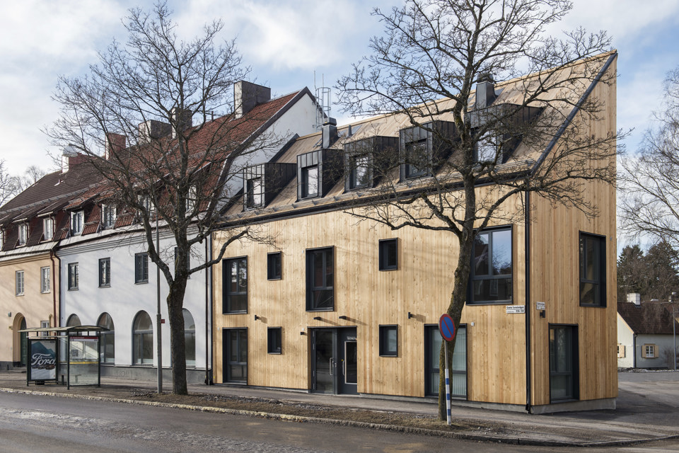 Ett mindre trähus med svarta fönsterpartier. Huset är byggt bredvid ett äldre vitt hus i likartad höjd.