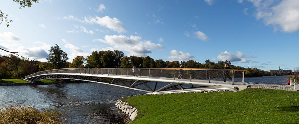 En gångbro i stål över vatten, ett par människor går över bron.